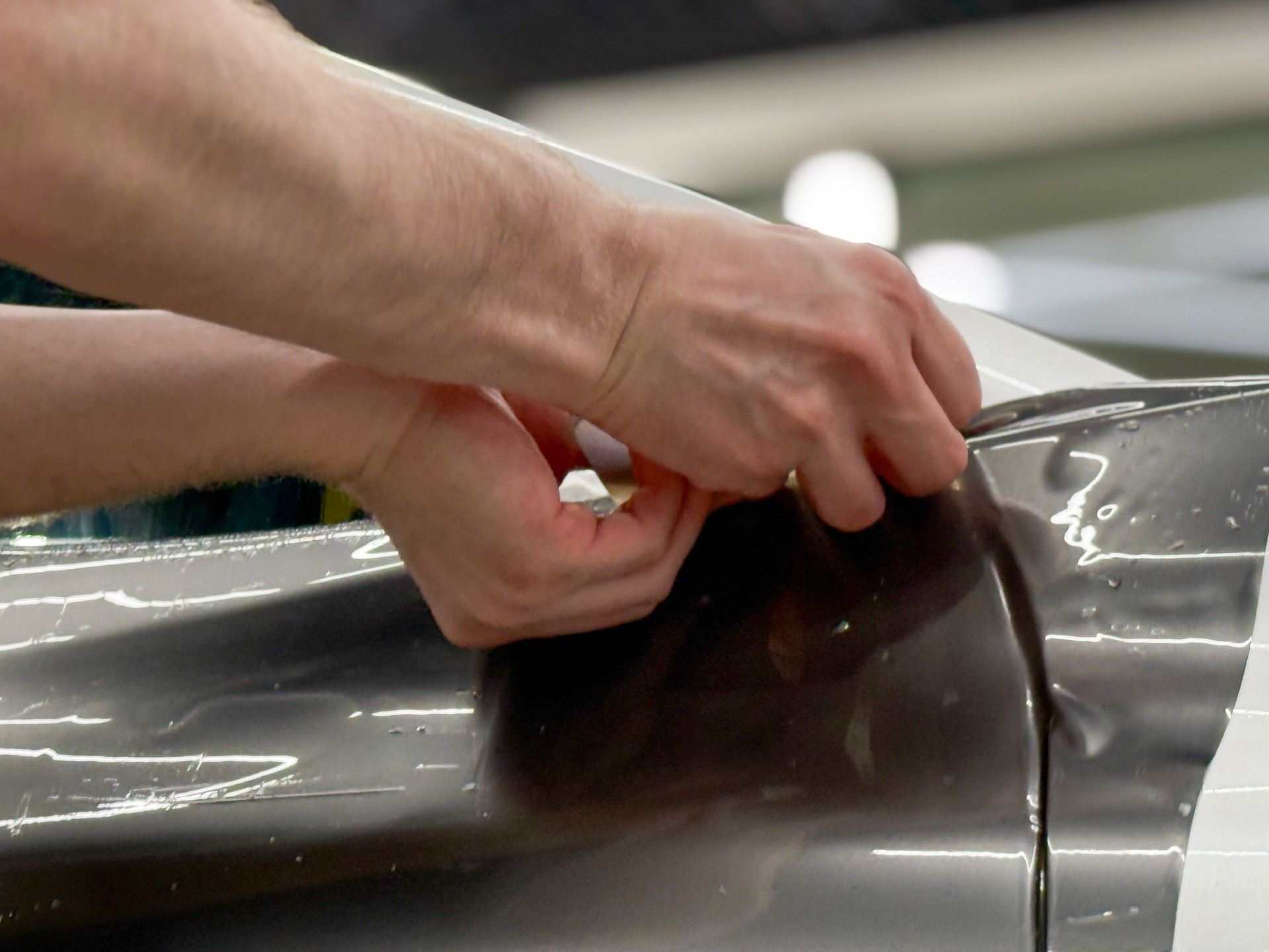 Car wrapping, detailing, tuning and styling. Detailer smoothes PPF. A car wrapping specialist applies a polyurethane film to the car. PPF protective film against chips and scratches.